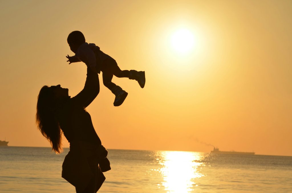 Mère qui porte son enfant devant la mer avec coucher de soleil